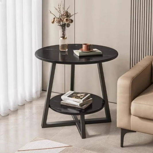 Round black side table with books and a vase in a living room setting.