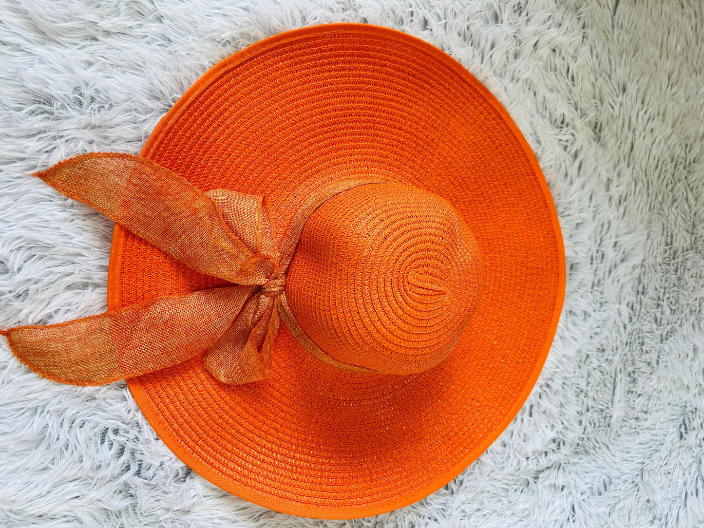 Orange straw hat with a bow on a white fluffy surface