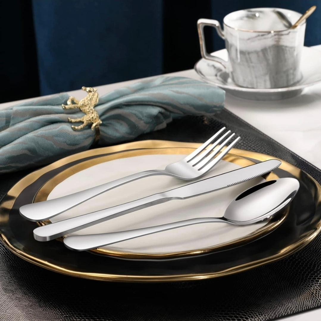 Silver cutlery set on a black and gold plate with a napkin and teacup in the background.