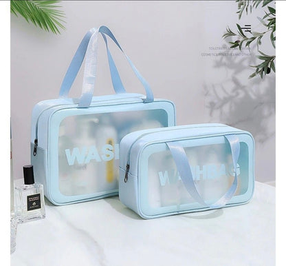 Two light blue transparent cosmetic bags with 'WASH' text on a white surface with a plant in the background.