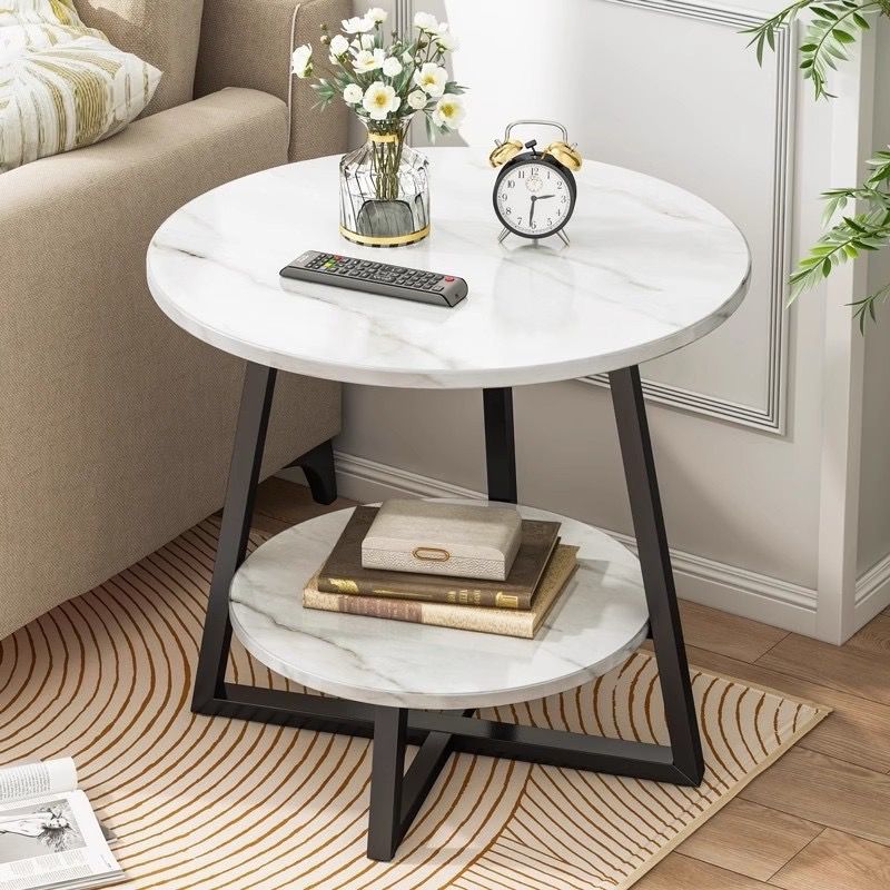 Round marble side table with black metal legs in a living room setting.