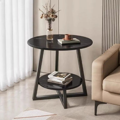 Round black side table with books and a vase in a living room setting.