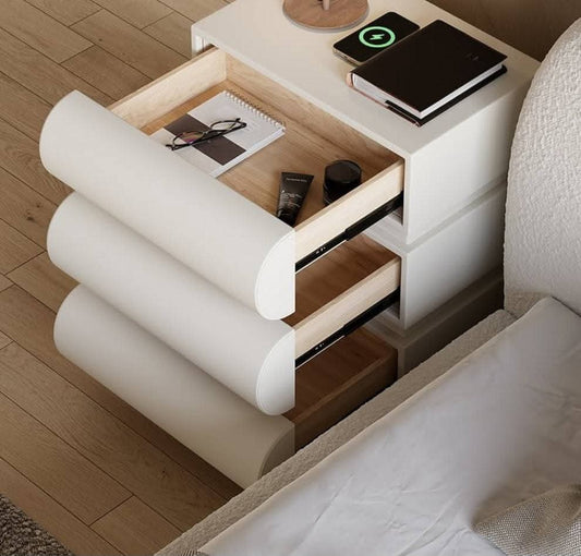 Modern nightstand with open drawer and items on top next to a bed.