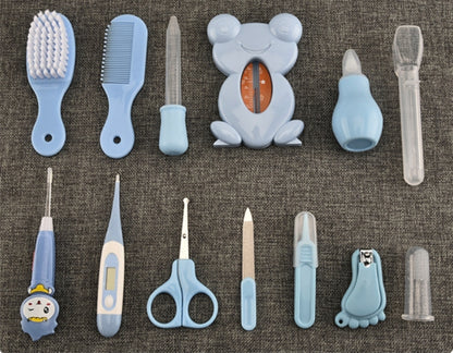 A set of baby grooming tools arranged on a textured gray fabric background, including a brush, comb, nail clipper, thermometer, scissors, nail file, and other light blue and clear plastic grooming accessories.