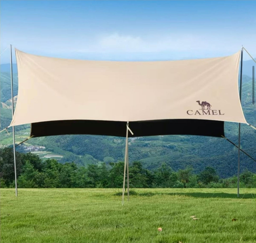 Beige camping tarp with Camel logo on a grassy field with mountains in the background