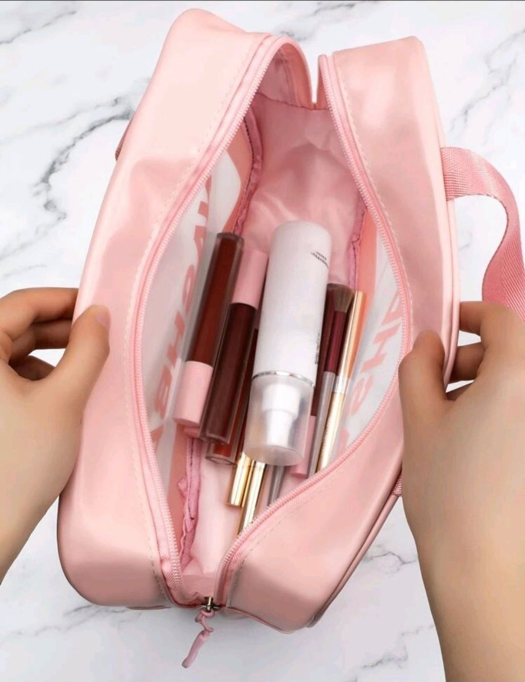 Pink cosmetic bag with makeup items on a marble surface